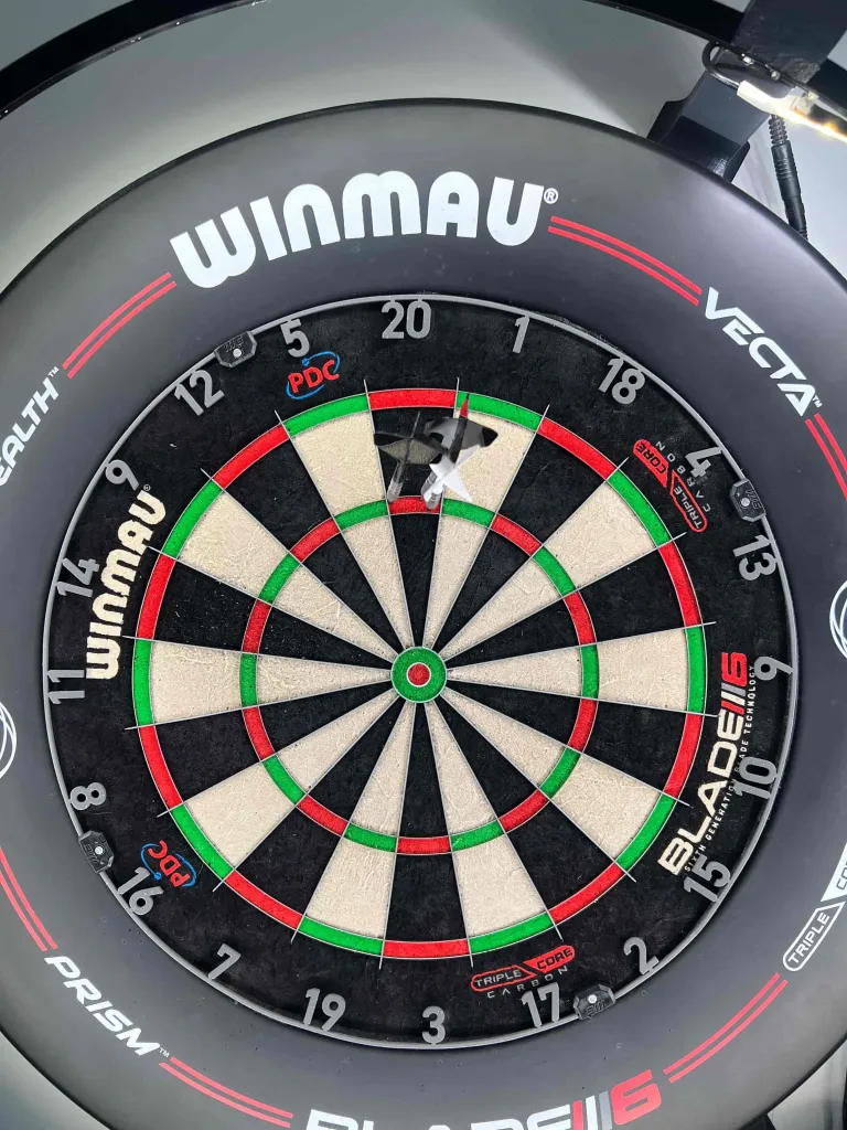 Three darts landed tightly together in the treble-20 ring of a Winmau dartboard, scoring 180.