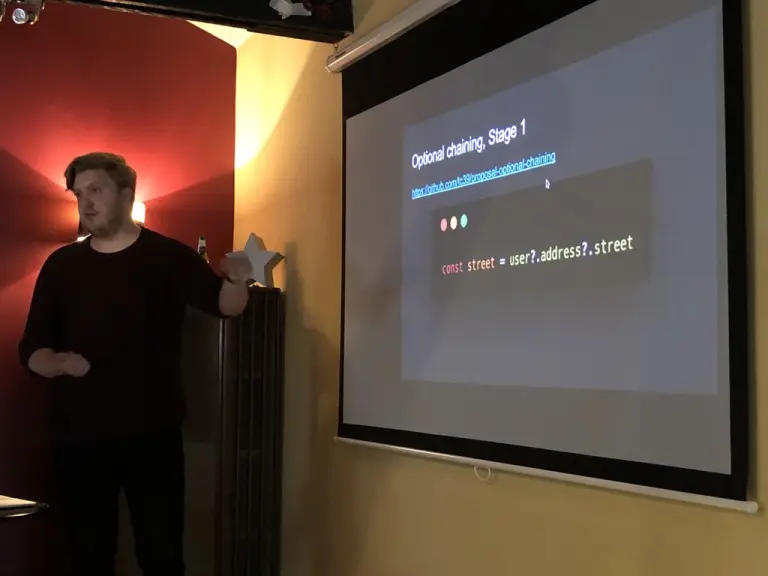 Craig gives a talk beside a projected slide titled Optional chaining, Stage 1, showing a JavaScript code example at JavaScript North East.